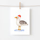 Postkarte Möwe A6 zeigt eine Möwe im Aquarellstil auf Naturpapier, mit gelbem Schnabel, grauen Flügeln und roter Mütze, aufgehängt an einer Kordel.