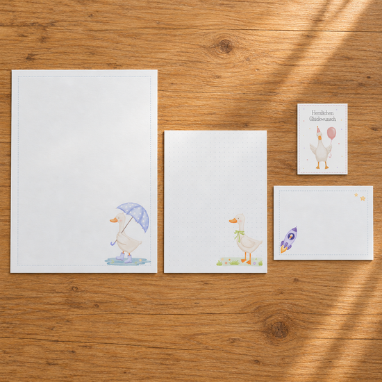 Papeterie-Set mit Gänsemotiven auf einem Holztisch mit Briefpapier, Notizpapier, Korrespondenzkarte und kleiner Grußkarte